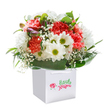 There is a celebratory spirit woven into every petal of this Harmondsworth-inspired bouquet, presented upright in a pristine white gift bag that hints at doorstep surprises along Stanwell Moor Road. The lush, ruffled petals of coral, peach, and deep red carnations mingle joyfully with white daisies that beam with refreshing yellow-green centers, together exuding warmth and optimism. Wisps of cloudlike baby's breath drift above the vibrant surface, creating a floating texture and an air of gentle sophistication. Peeking through lush greenery on one side, closed purple-tinged buds add a touch of anticipation and visual intrigue. Each flower nestles among broad, glossy green leaves that form a protective cradle-an expert arrangement that balances lush fullness with artistry, reminiscent of bouquets hand-tied at Flower Delivery Harmondsworth. Set against a flawless white background, the composition has a modern clarity, every hue and detail designed to stand out and uplift. The bouquet's presentation-in an elegant bag with white ribbon handles-underscores both convenience and care, making it ideal for birthdays, anniversaries, or to offer neighbours a delightfully fresh gesture of friendship. Every stem and flourish speaks to a florist's local pride and the joy of thoughtful giving.
